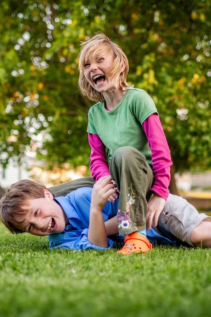 Two children laughing while playing on grass.